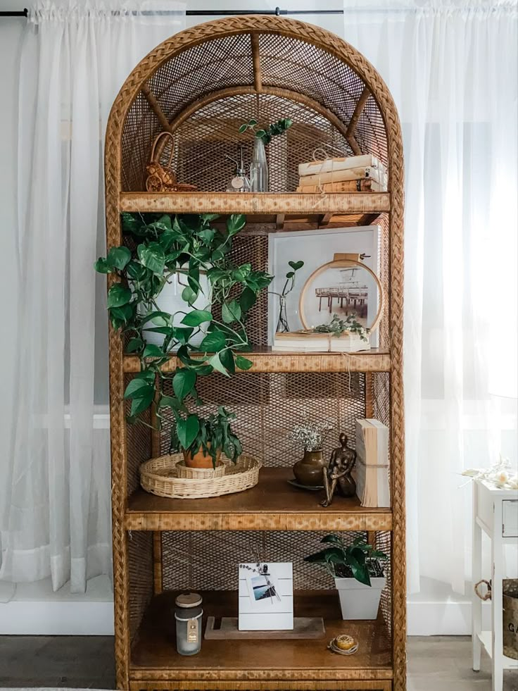 a wicker bookcase with plants and pictures on it in front of a window