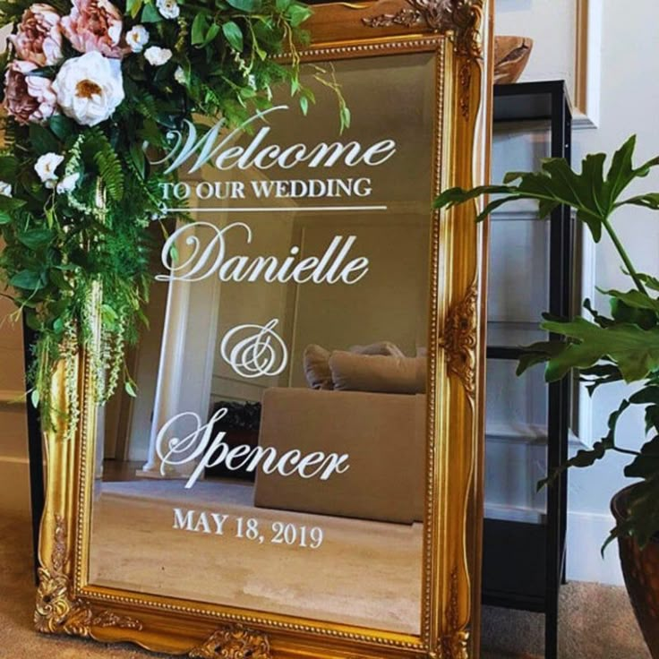 a gold framed mirror sitting next to a potted plant and vase filled with flowers