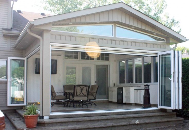 a screened porch with chairs and tables on the steps leading to an outside dining area