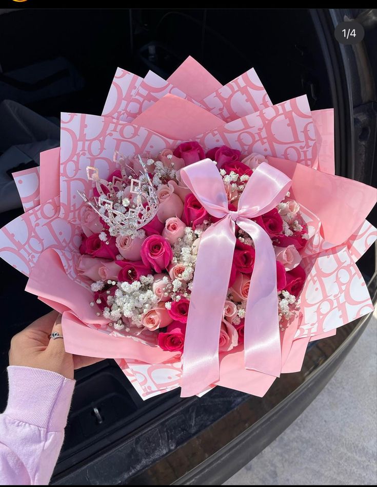 someone holding a bouquet of flowers in front of a car door with pink ribbons on it