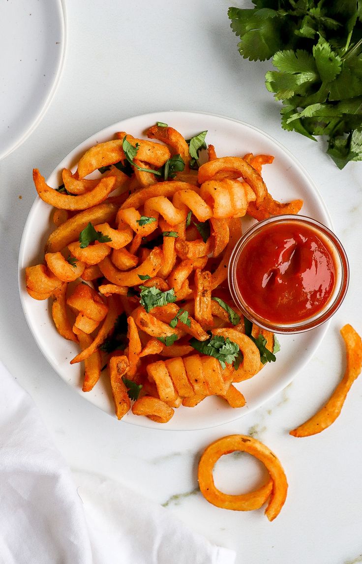 a white plate topped with cheesy fries next to a bowl of ketchup