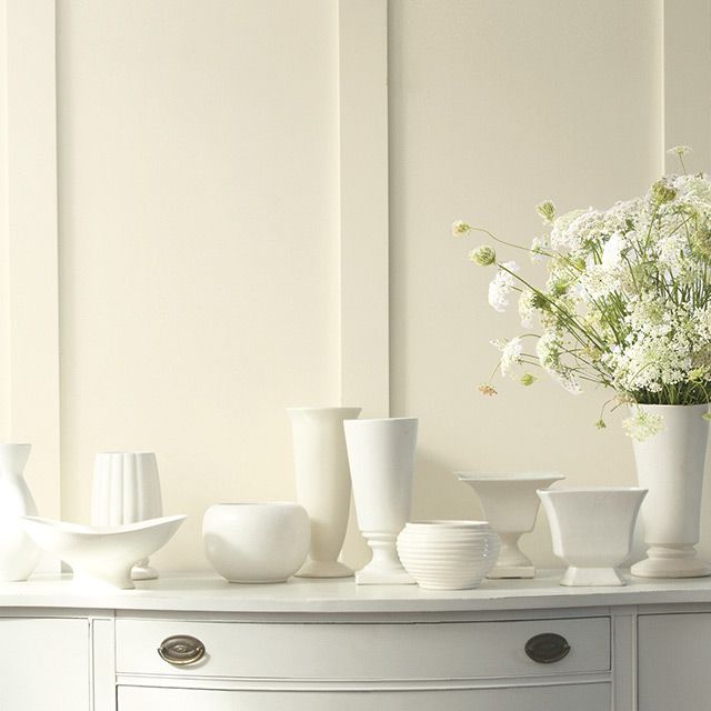 white vases and bowls sit on top of a dresser next to a flower arrangement