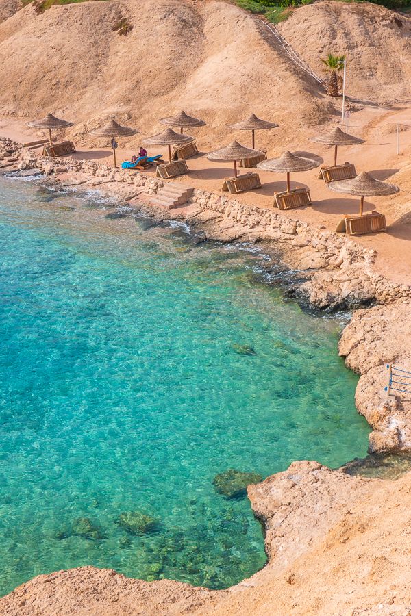 there are umbrellas and chairs on the beach by the water's edge,