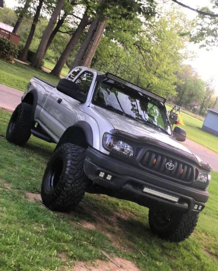 a silver truck parked in the grass near trees