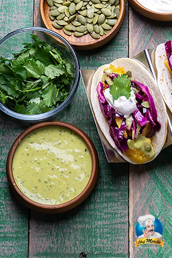 three tacos and two bowls of vegetables on a wooden table with green sauces