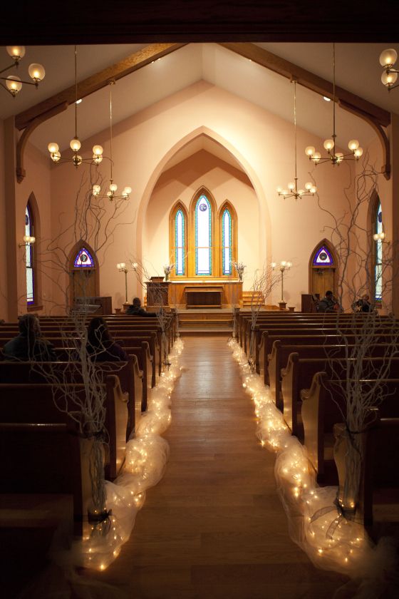 an empty church filled with lots of pews and decorated with branches, lights and candles