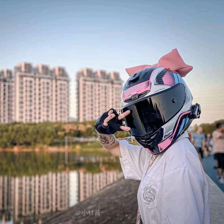 a person wearing a helmet with a pink bow on their head standing next to a body of water