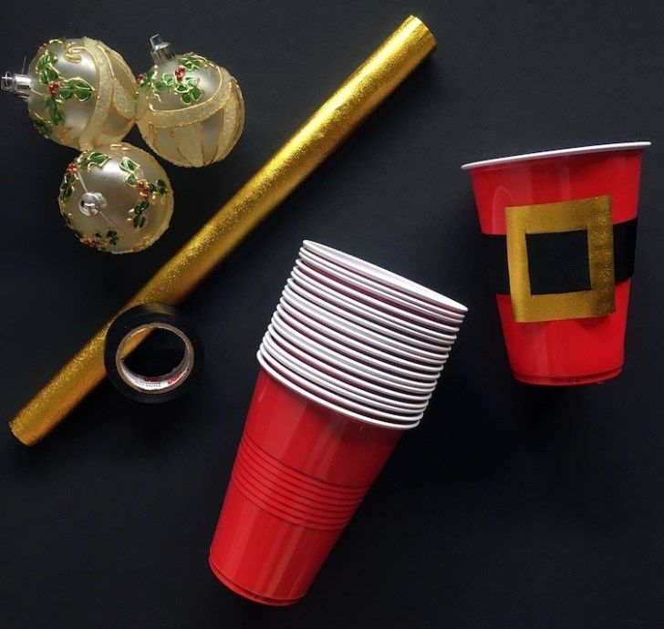 red cups with gold rims and decorations on black tablecloth next to christmas tree ornament