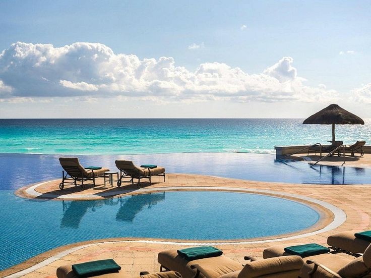 an empty swimming pool with lounge chairs and umbrellas next to the water's edge