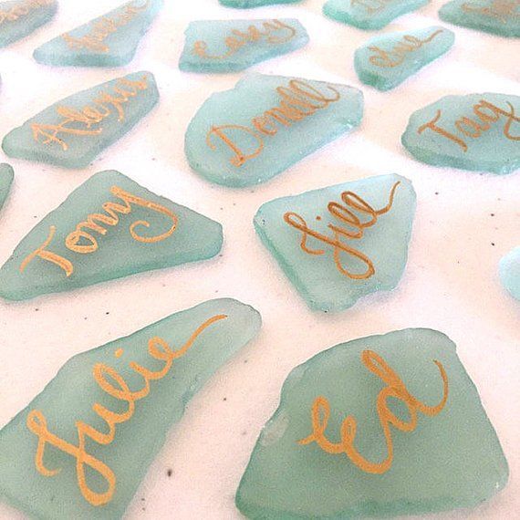 sea glass rocks with writing on them sitting on a white tablecloth covered in gold foil