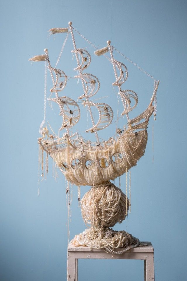 a sculpture made out of string and rope on top of a wooden table against a blue wall