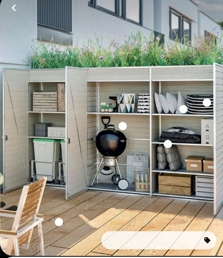 an outdoor storage unit with plants on the top and shelves below, in front of a building