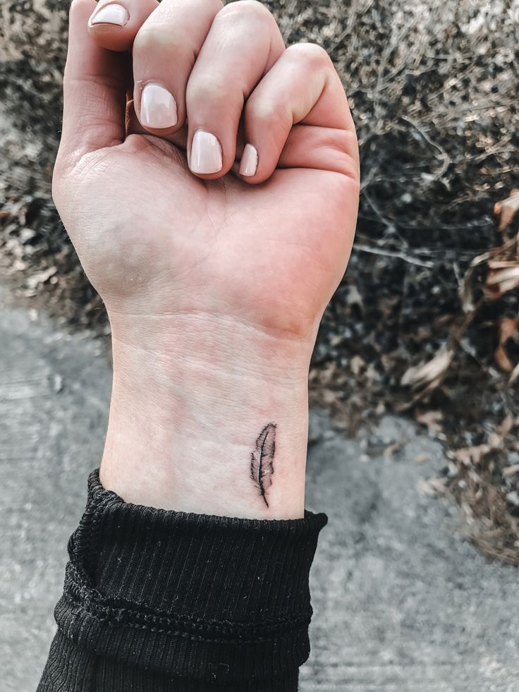 a woman's hand with a small feather tattoo on her left wrist and the other arm