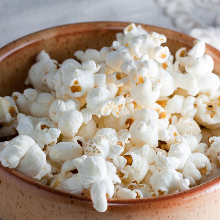 a brown bowl filled with white popcorn on top of a wooden table next to a napkin