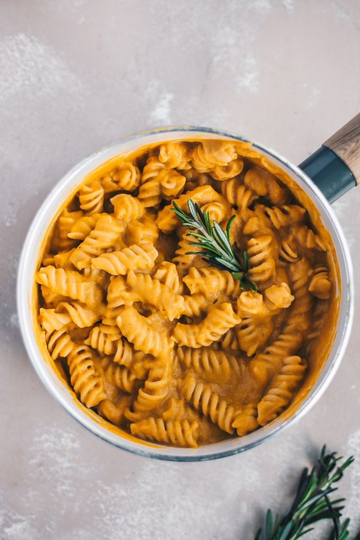 a pot filled with pasta and sauce on top of a white counter next to rosemary sprigs