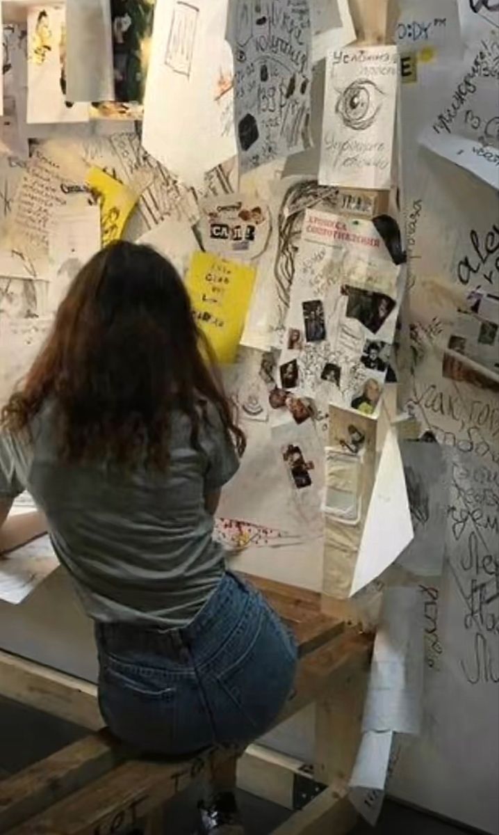 a woman sitting at a table with papers on it and writing on the wall behind her