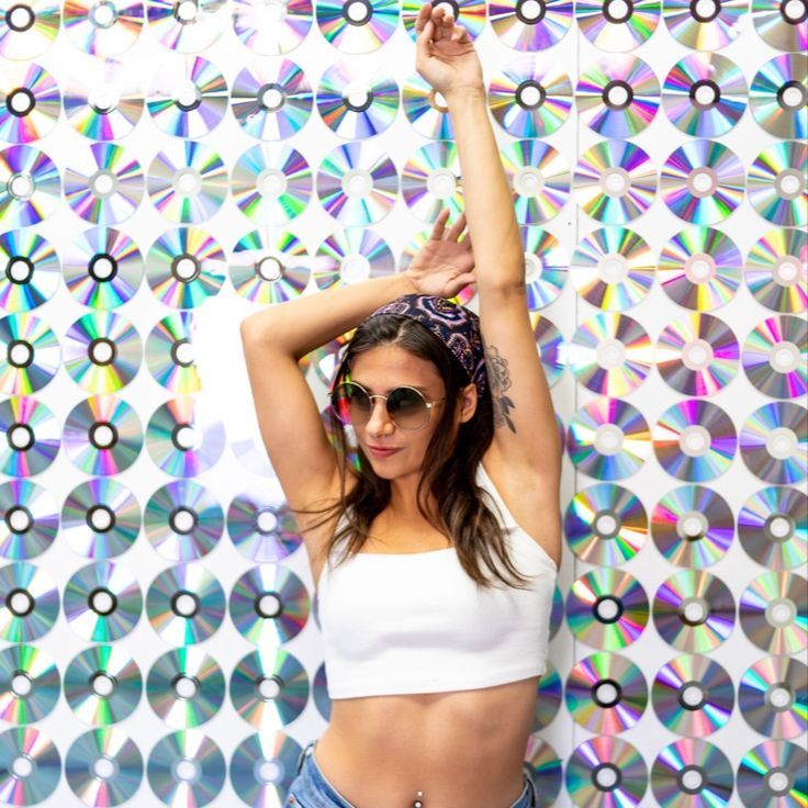 a woman in white top and blue jeans standing next to a colorful wall