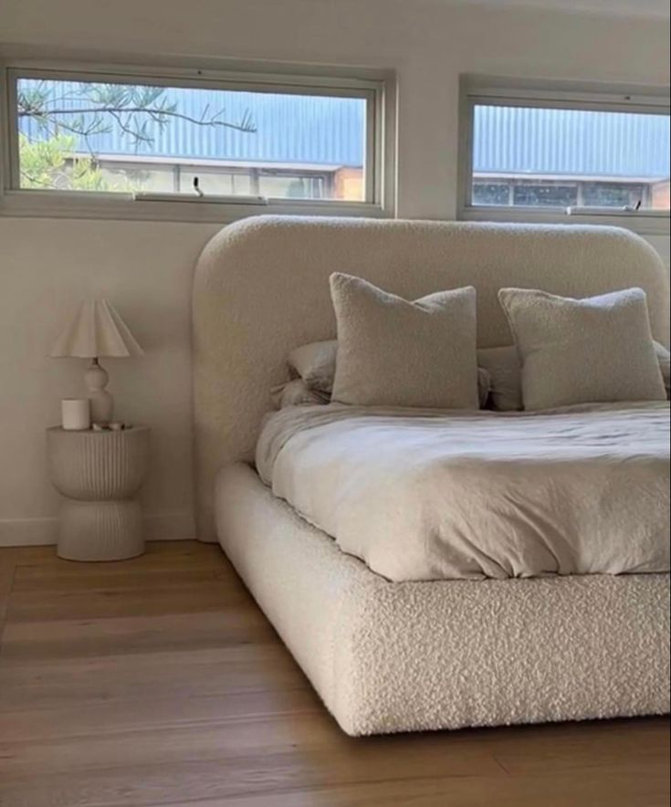 a white bed sitting in the middle of a bedroom next to two lamps and windows