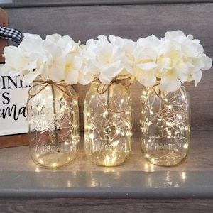 three mason jars filled with white flowers and fairy lights