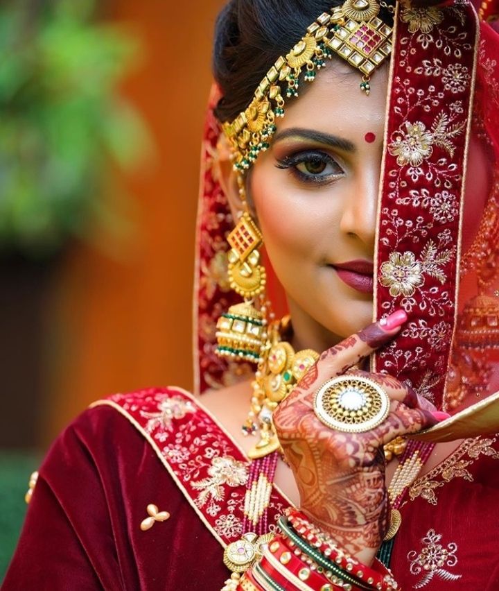 a woman wearing a red and gold bridal outfit with her hands on her face