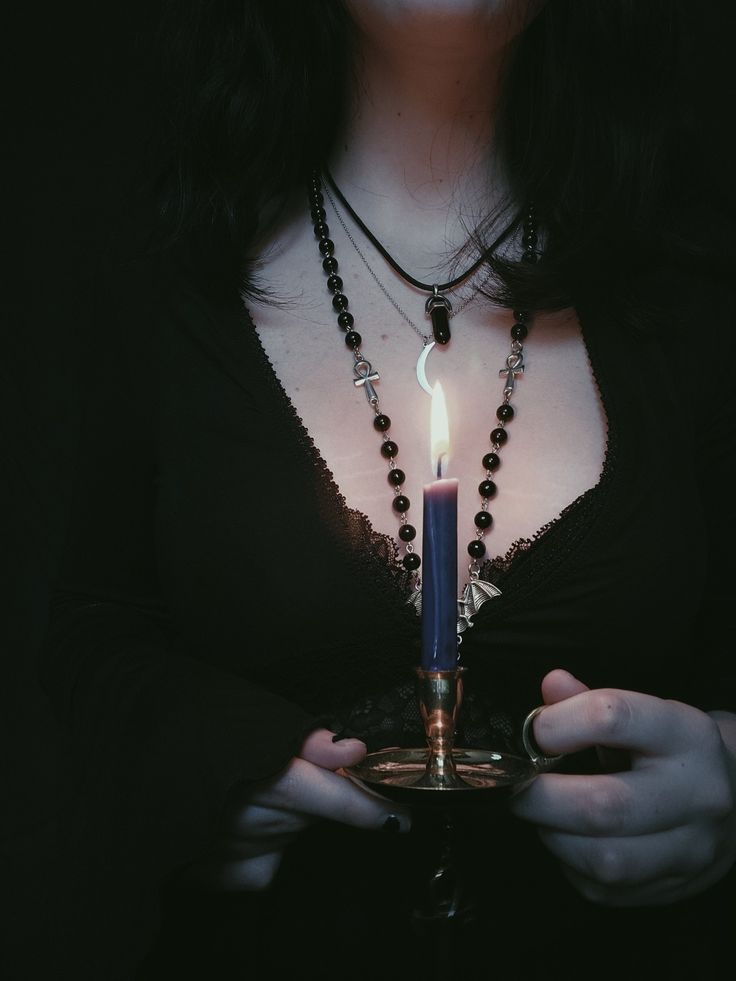 a woman holding a candle in her hands with beads around her neck and necklace on