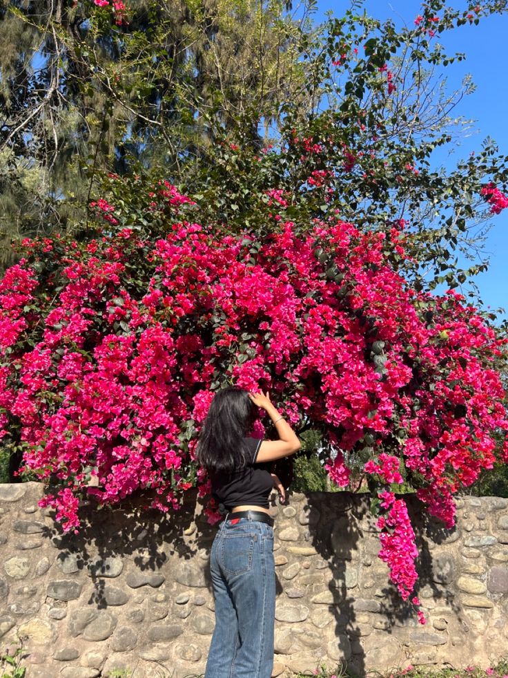 a woman standing in front of a tree with pink flowers