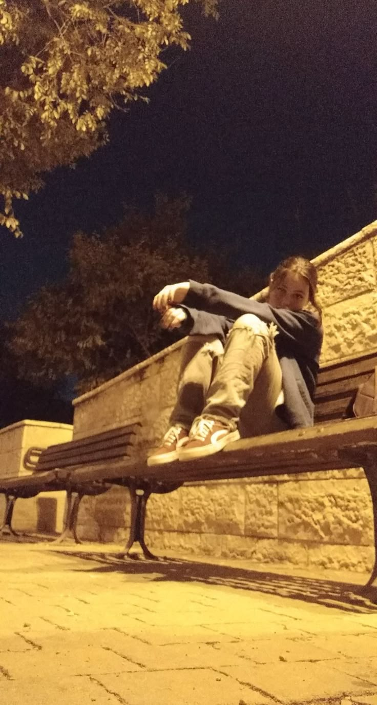 a man sitting on top of a wooden park bench next to a tree at night