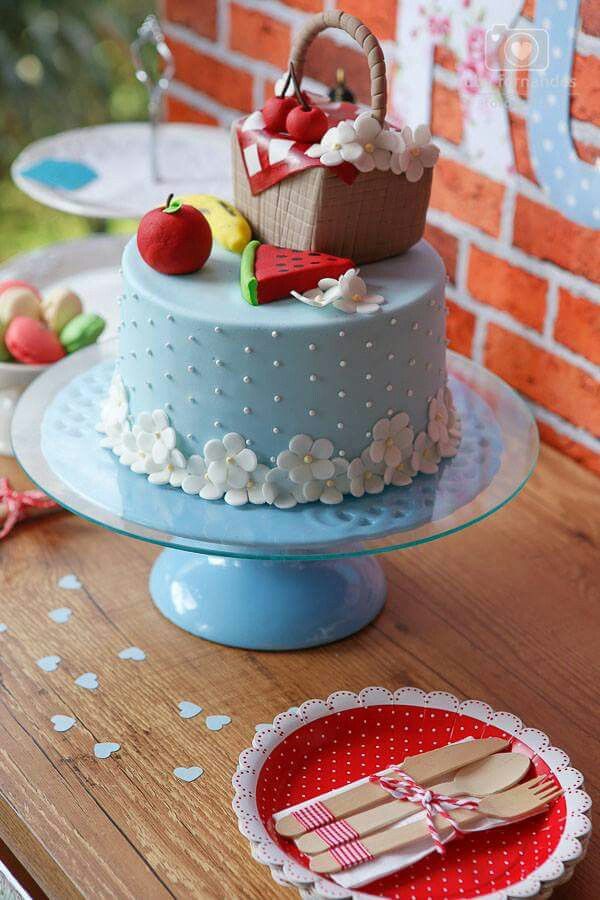 there is a blue cake with white flowers on the top and an apple in a basket