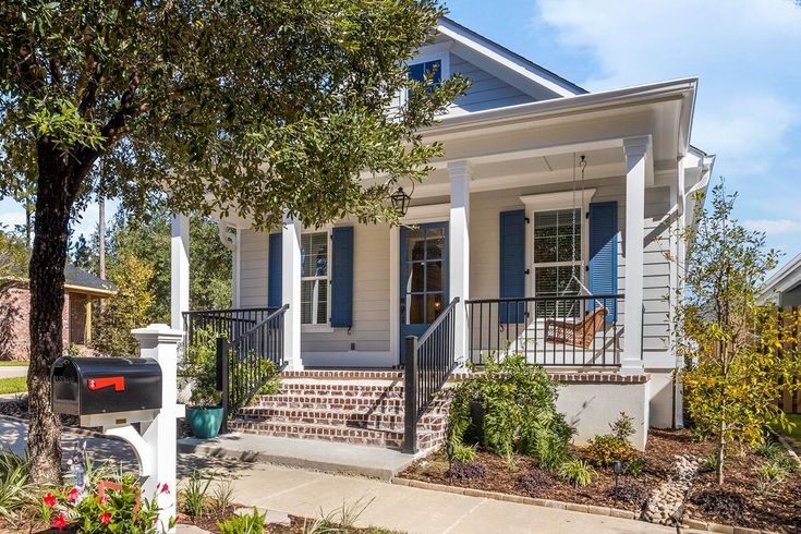 a white house with blue shutters and a mailbox in the front yard on a sunny day