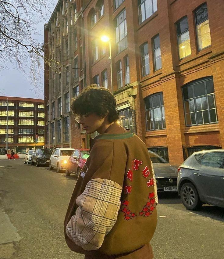 a man walking down the street in front of tall buildings with cars parked on both sides