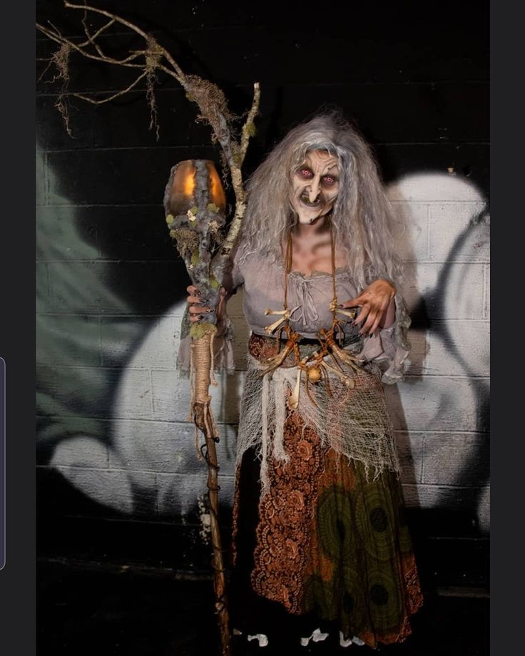 a woman dressed up as a zombie holding two torches in front of a painted wall