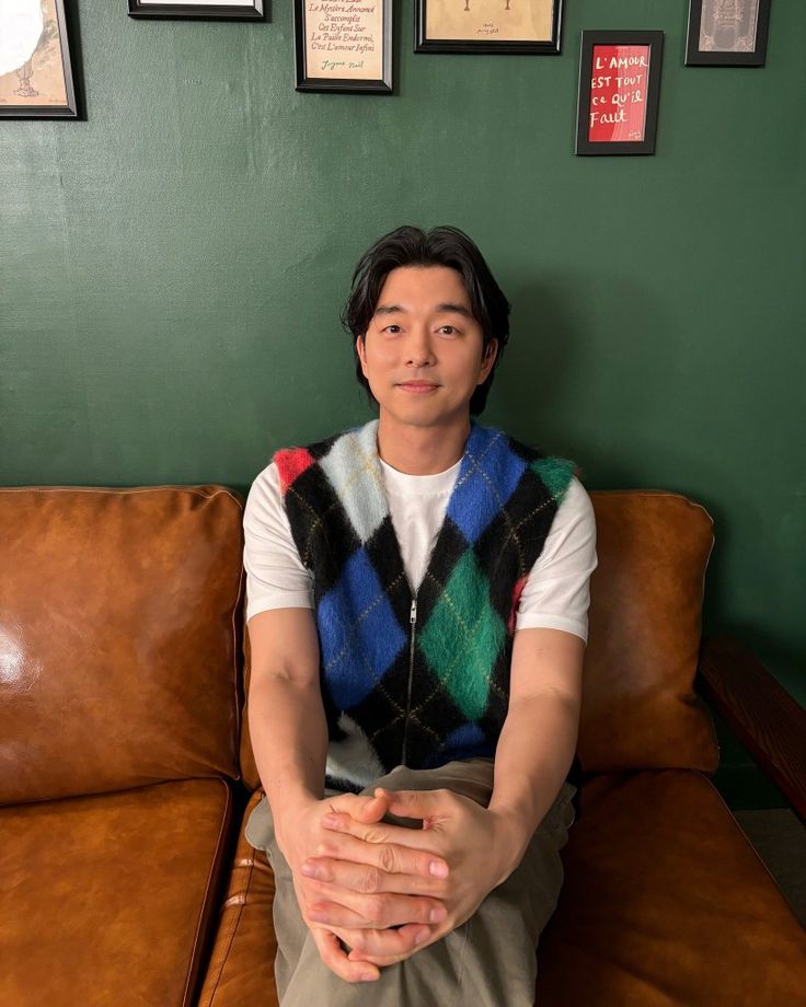 a man sitting on top of a brown couch next to a wall covered in pictures