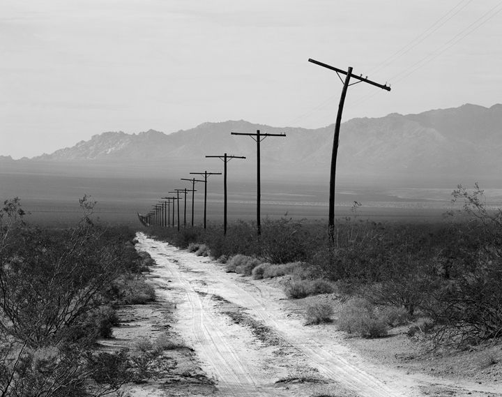 an empty dirt road with telephone poles and mountains in the background, black and white photo