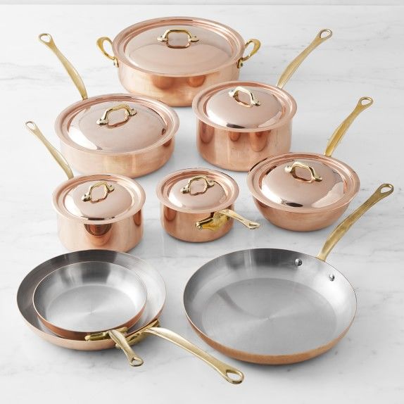 copper pots and pans with gold handles on a marble countertop in front of white background