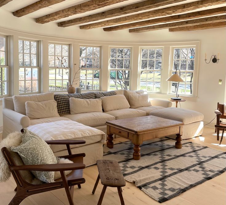 a living room filled with furniture and windows covered in wood beamed ceilinging next to a white couch