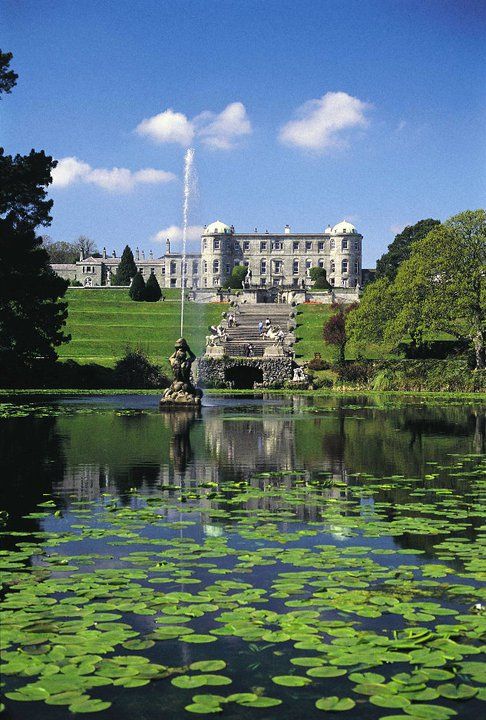 a large building sitting on top of a lush green field next to a lake filled with lily pads