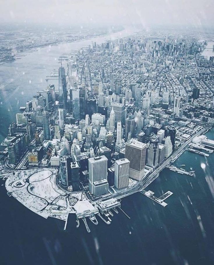 an aerial view of a large city in the middle of the ocean with snow falling on it