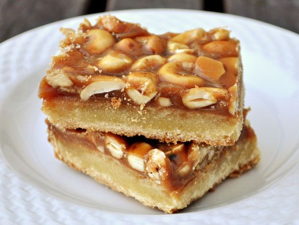 two pieces of dessert sitting on top of a white plate with nuts and caramel toppings