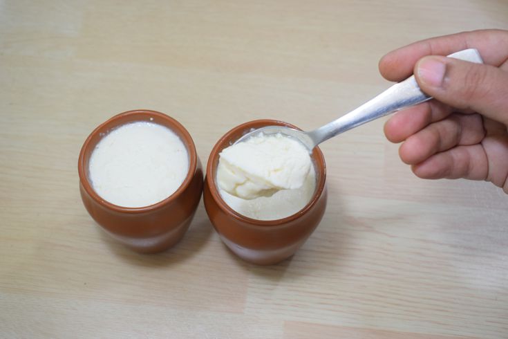 a person is spooning some cream into two small brown cups on a wooden table