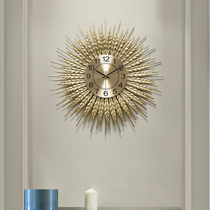 a gold clock on the wall next to a candle and vase with a candle in it