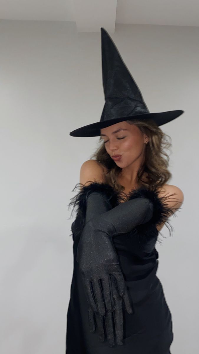 a woman wearing a witches hat and black gloves with her hands on her chest,