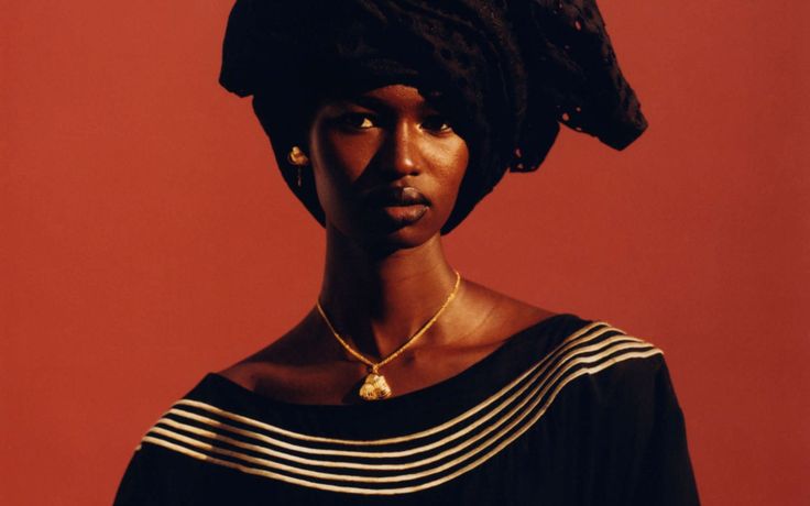 a woman wearing a black dress and gold necklace with a bird on it's head