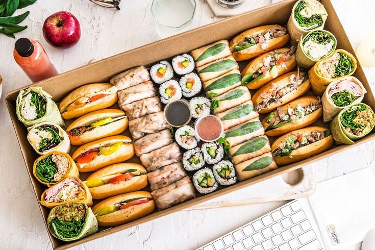 a box filled with assorted sushi and rolls next to a keyboard on a table