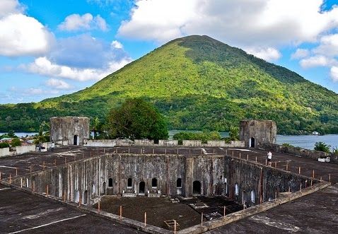 an old building in front of a mountain with water and trees on it's sides