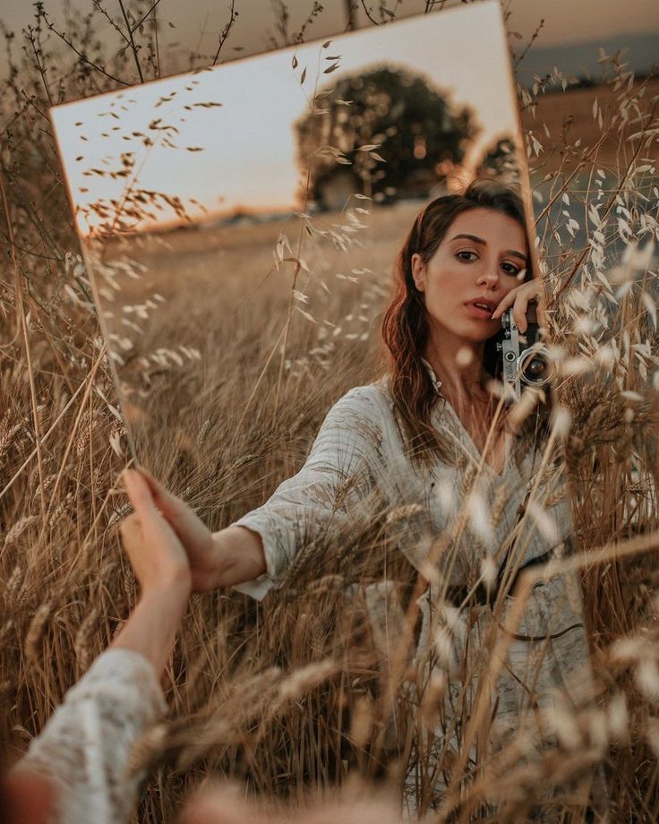 a woman standing in tall grass holding a cell phone to her ear and taking a selfie