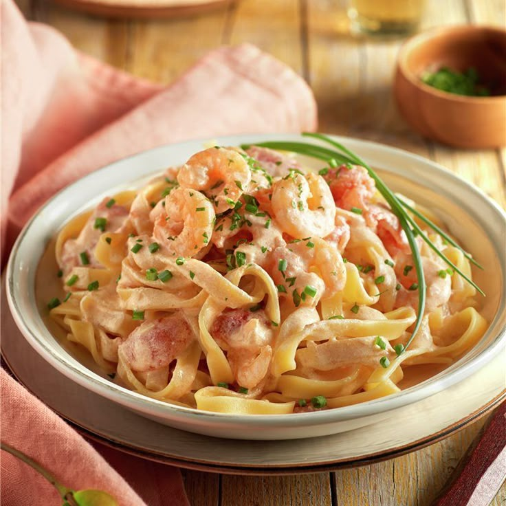 a white plate topped with pasta covered in sauce and shrimp on top of a wooden table