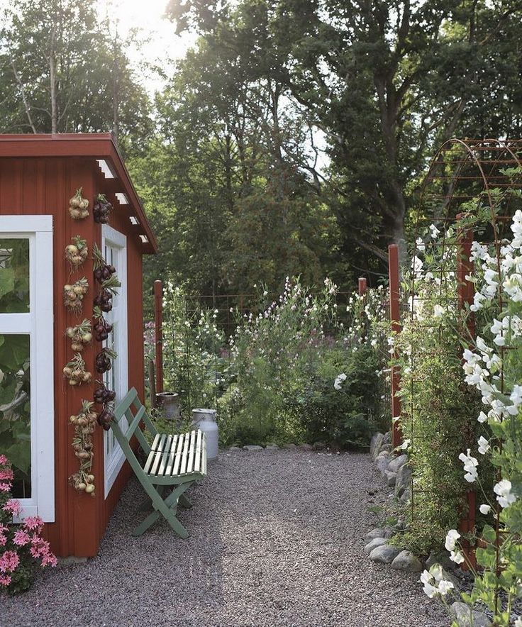 a wooden bench sitting next to a red shed with flowers growing on it's side