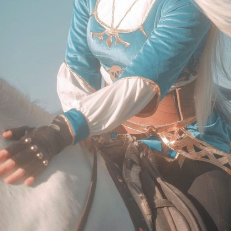 a woman riding on the back of a white horse wearing a blue and white outfit