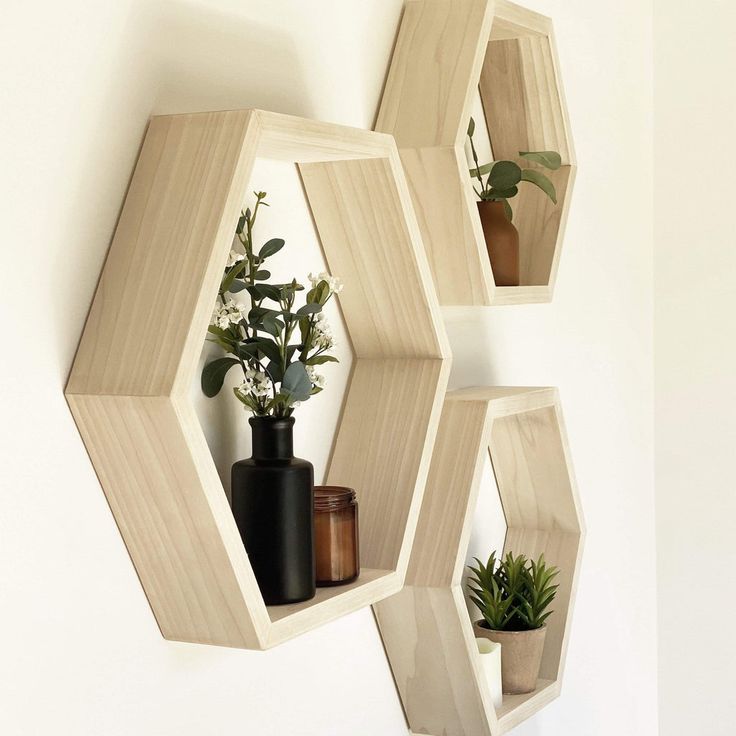 three wooden hexagonal shelves with plants and vases on them against a white wall