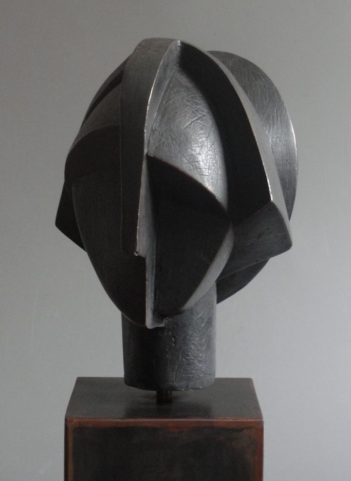 a black sculpture sitting on top of a wooden block in front of a gray wall